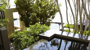Un área de piscina exterior moderna con superficie de agua cristalina, rodeada de exuberante vegetación y árboles.