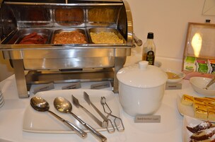 Buffet com pratos identificados, incluindo linguiça, ovos mexidos e ovos cozidos.