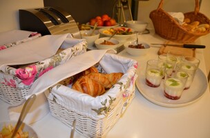 Disposição de mesa para café da manhã com croissants, frutas e bebidas.