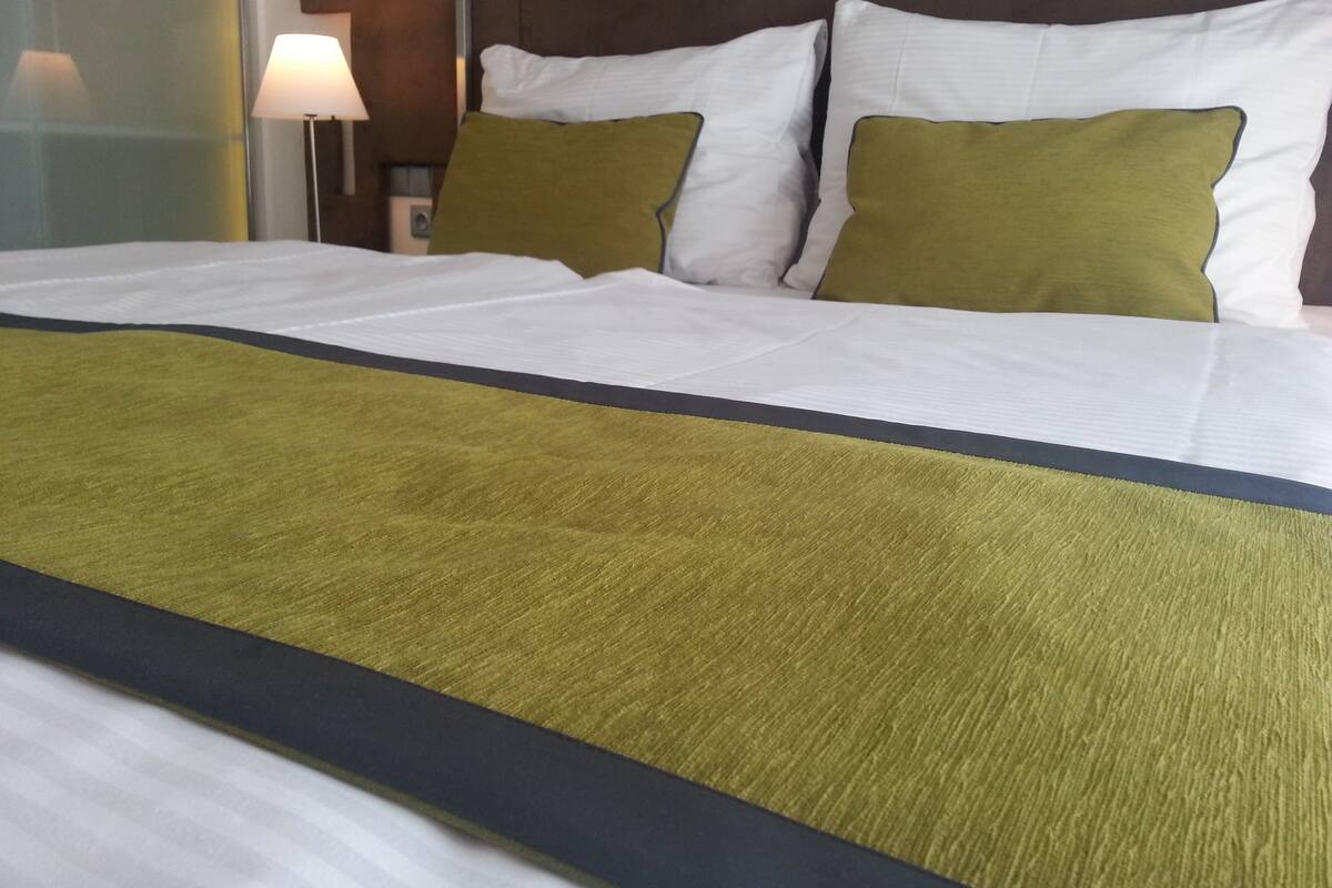 A neatly made bed with white and green pillows and a green and black bedspread.