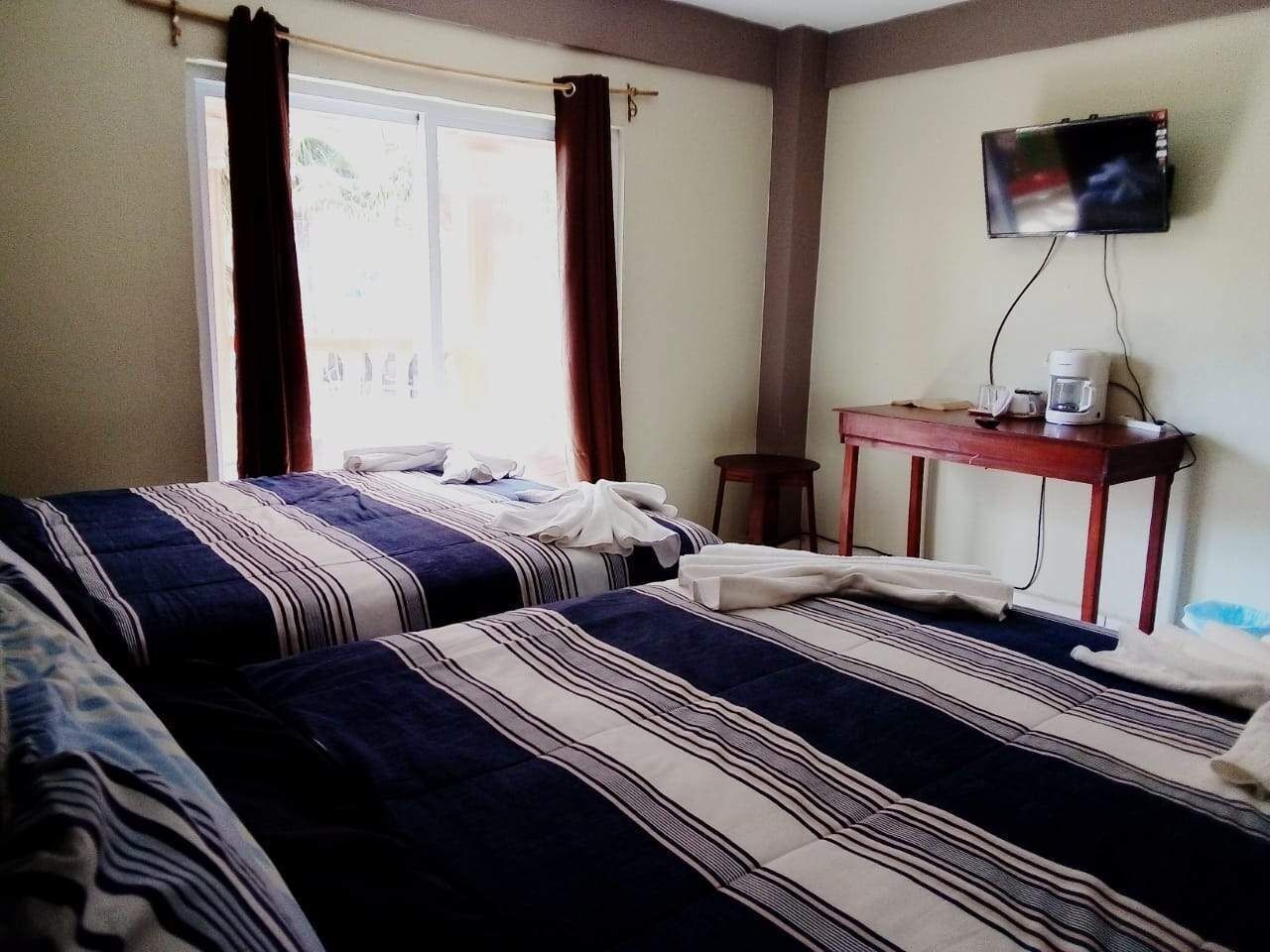 A hotel room with two beds, a TV, a coffee maker, and a window with curtains.