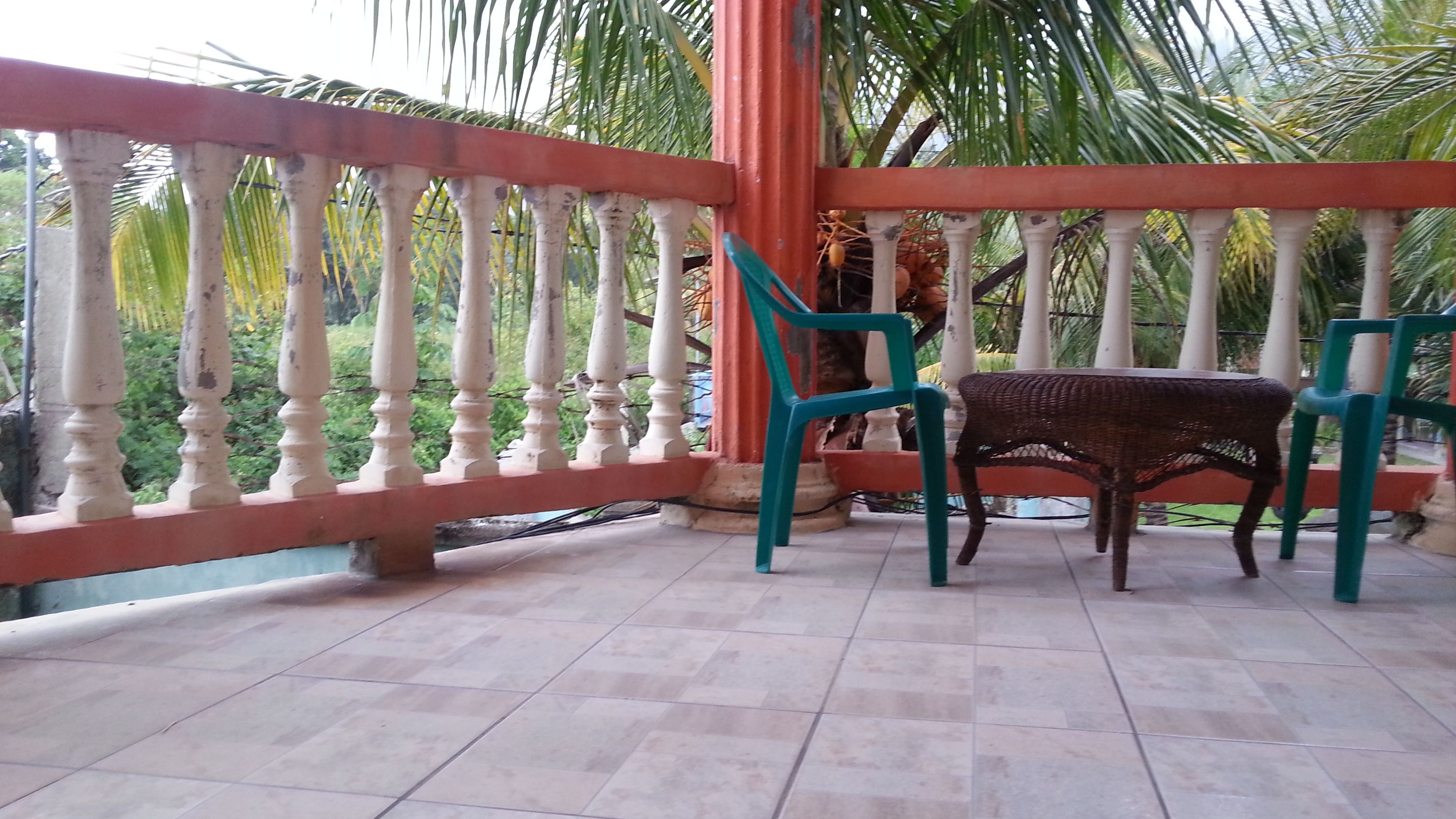 A balcony with a tiled floor, a wicker table, and two chairs.