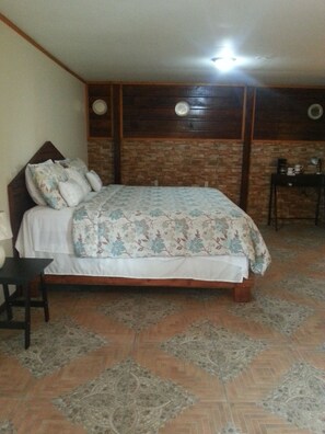 Un dormitorio con cama, mesita de noche, una pequeña mesa y un reloj de pared.