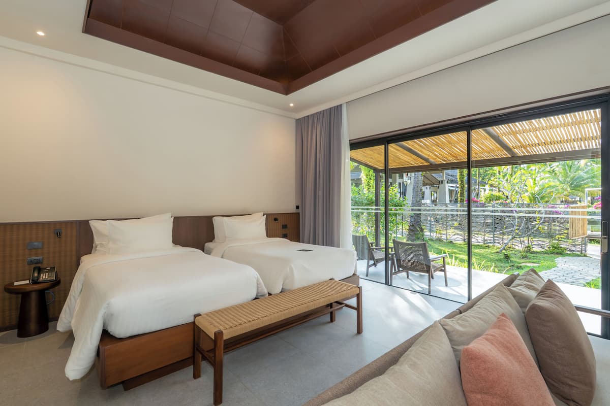 Habitación de hotel con dos camas, un banco, una mesita con un teléfono y vistas al área exterior.