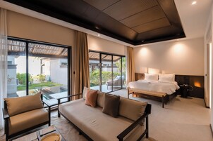 Una habitación de hotel moderna con una cama grande, un sofá y un balcón con vistas al jardín.