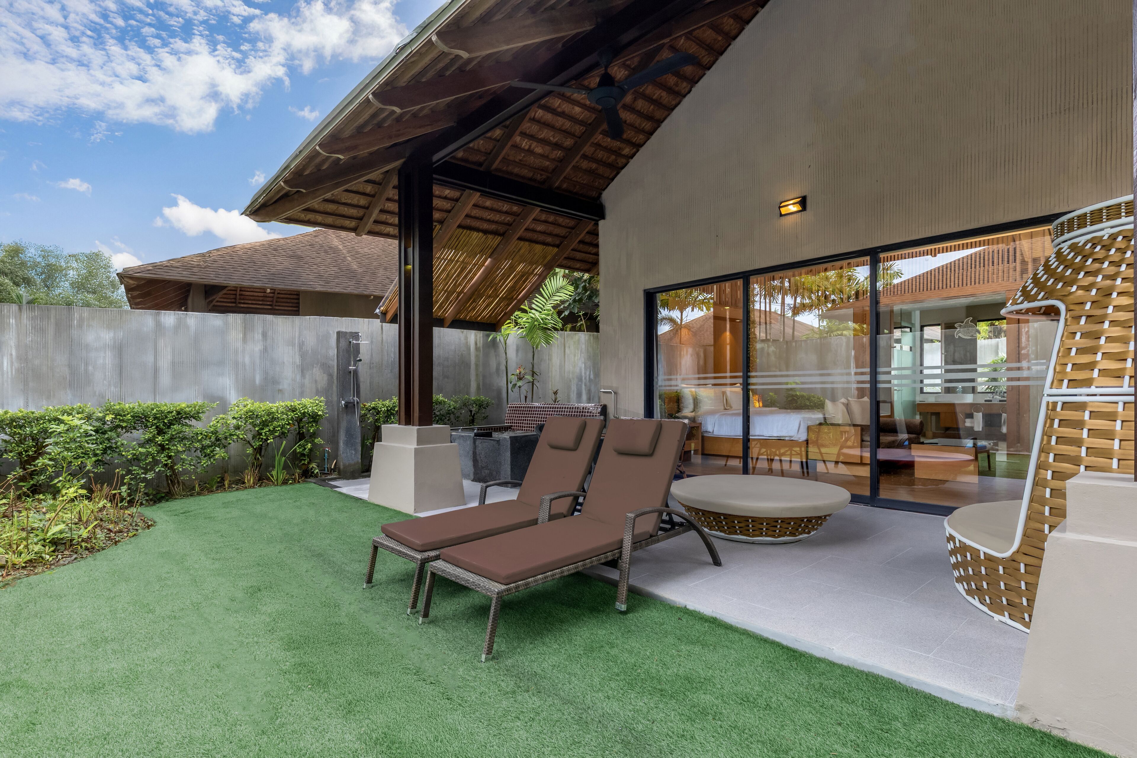 A modern outdoor patio with a lounge chair and a round table, a covered area with a ceiling fan, and a glass door leading to an interior space.