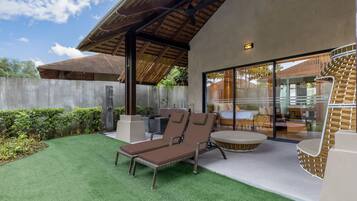 A modern outdoor patio with a lounge chair and a round table, a covered area with a ceiling fan, and a glass door leading to an interior space.