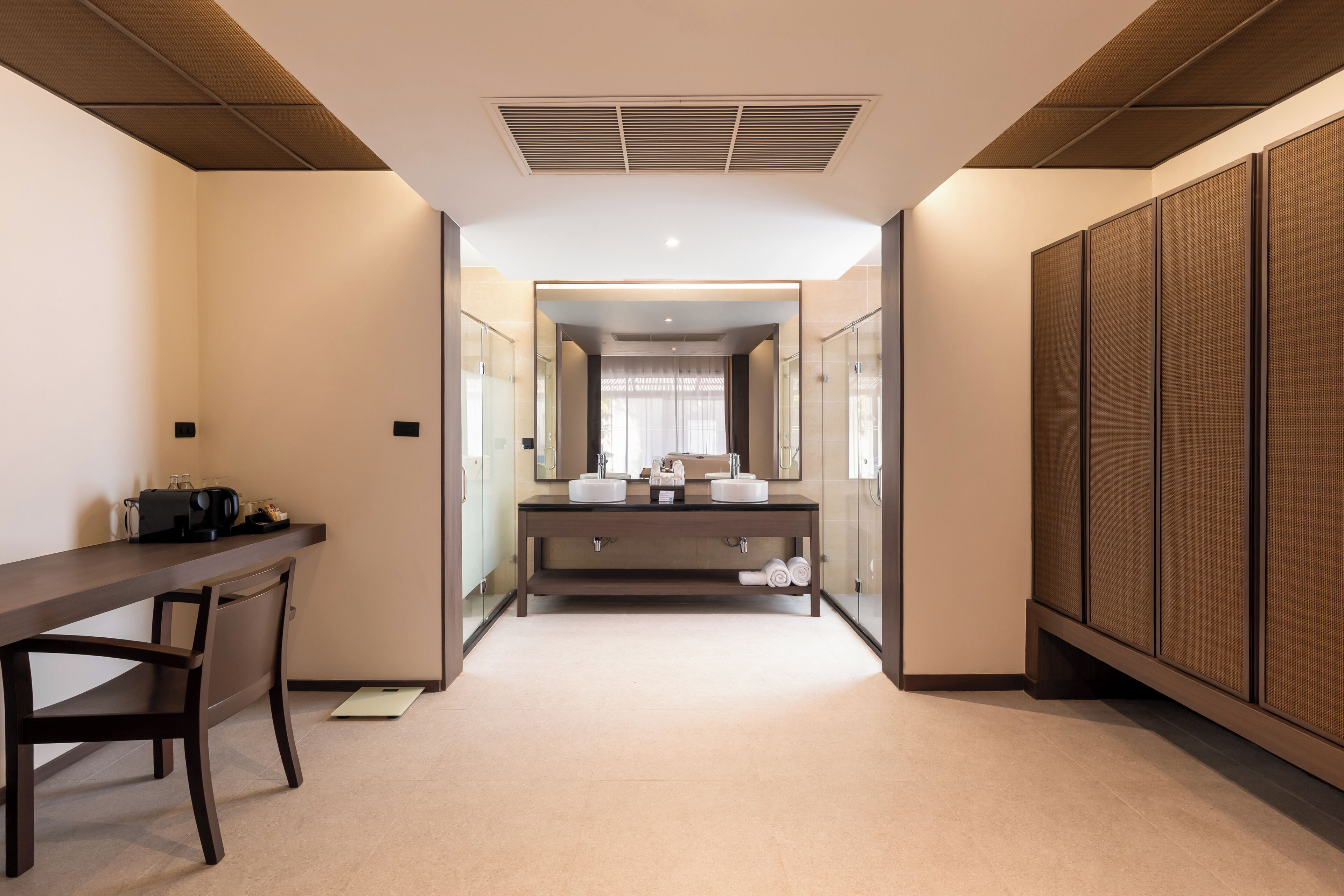 A modern hotel room with a long desk, a chair, a large mirror, and a walk-in closet.