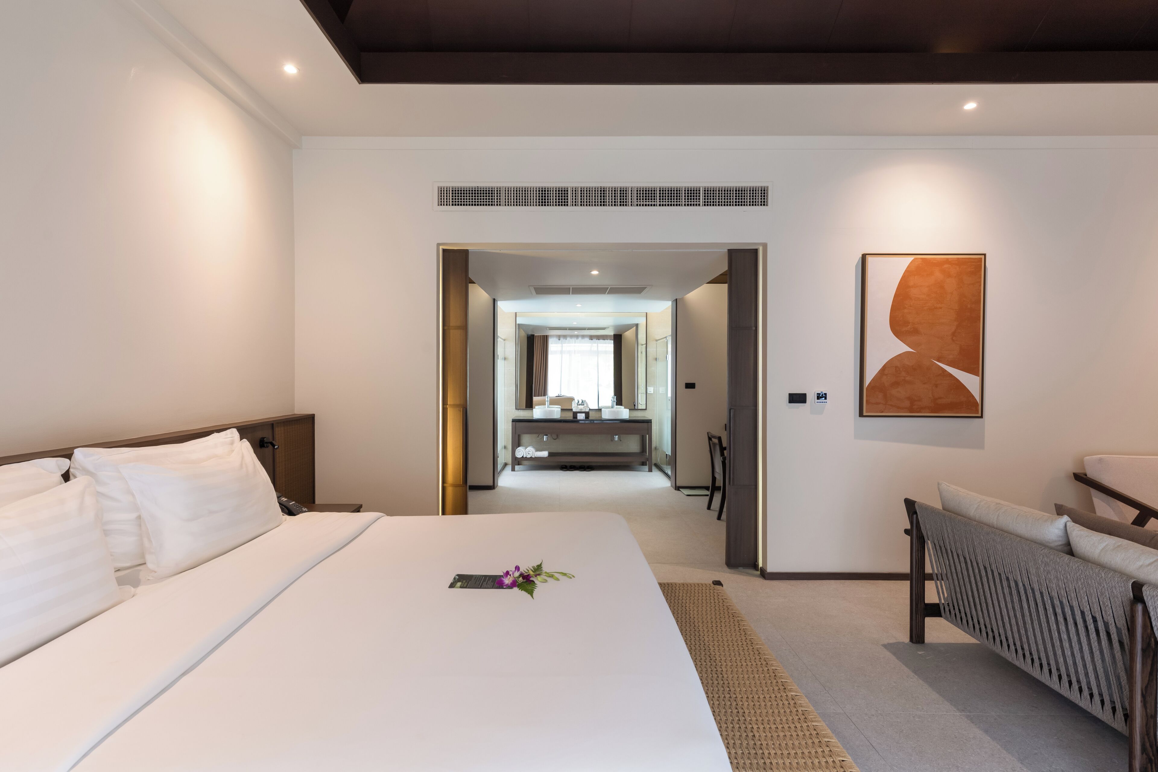 A modern hotel room with a large bed, a sitting area, and a view into the bathroom.