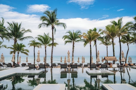 A poolside area with lounge chairs and umbrellas, palm trees, and a view of the ocean.. ananea Beyond Khaolak