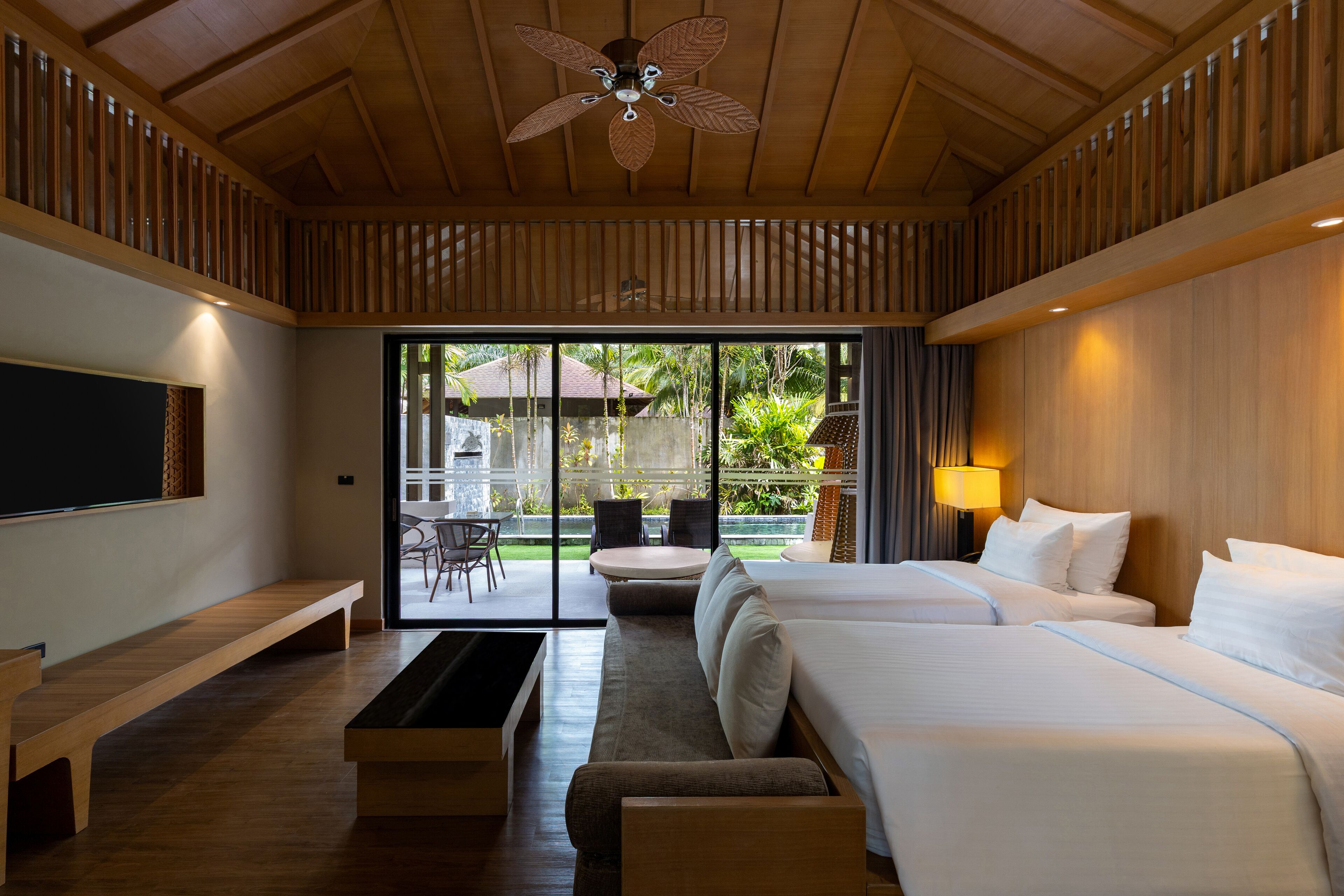 A hotel room with a large bed, a sofa, a TV, and a ceiling fan.