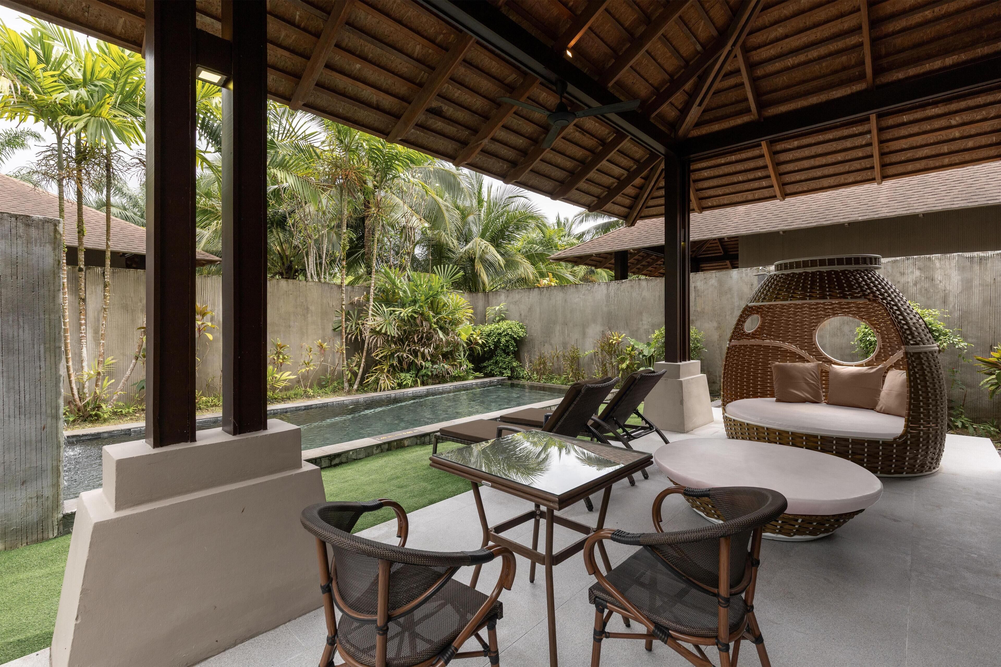 Un espacio al aire libre cubierto con piscina, sillones de descanso y un sofá de mimbre.