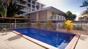 A rectangular swimming pool with a tiled edge, surrounded by a white metal fence. - Sundale Motel (Southport)