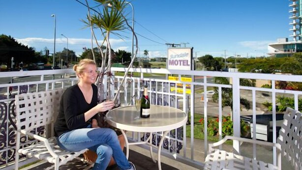 A woman sitting at a table with a bottle of wine on a balcony with white railings and a sign for 'Sundale Motel' in the background. - Sundale Motel (Southport)