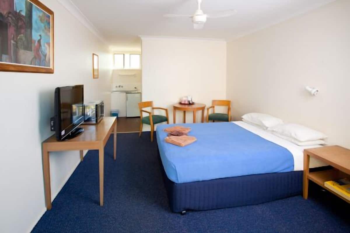 Quarto de hotel com cama, escrivaninha com televisão, cadeira e uma mesinha.