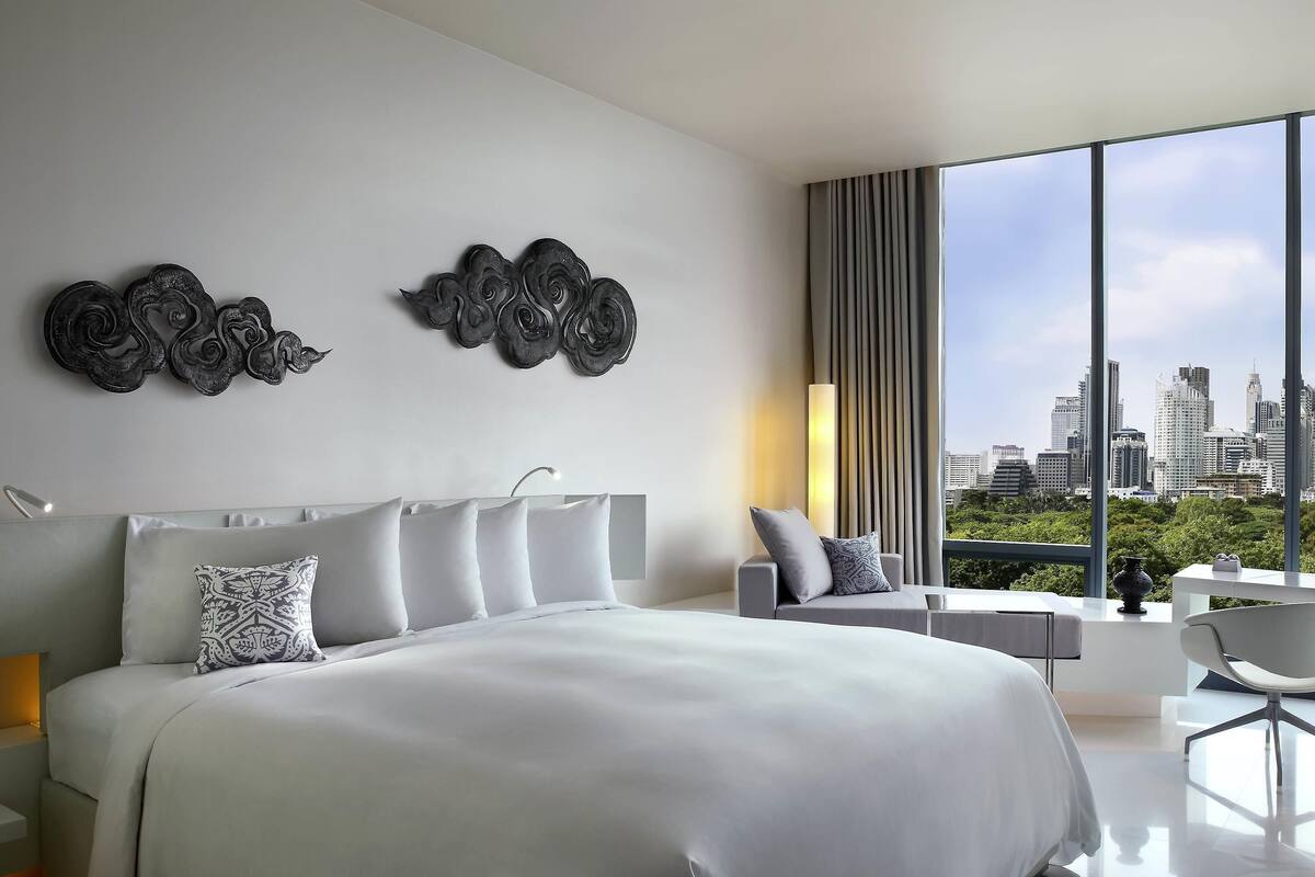 A modern bedroom with a large bed, a desk, and a view of a cityscape.