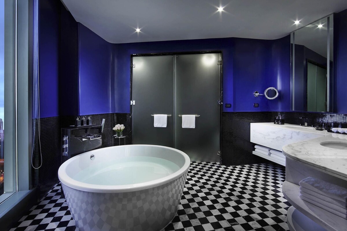 A modern bathroom with a freestanding bathtub, a large mirror, and a checkered floor.