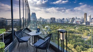 A balcony with a city view, two wicker chairs, a small table, and a tablet. - SO/ Bangkok (Bangkok)