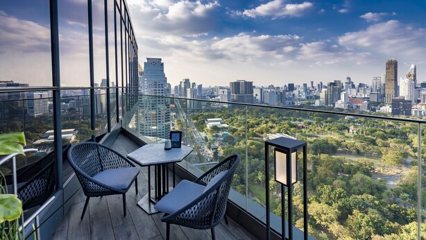A balcony with a city view, two wicker chairs, a small table, and a tablet. - SO/ Bangkok (Bangkok)