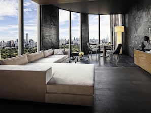 A modern living room with a large sofa, a dining table, and a view of a city skyline through large windows. - SO/ Bangkok (Bangkok)