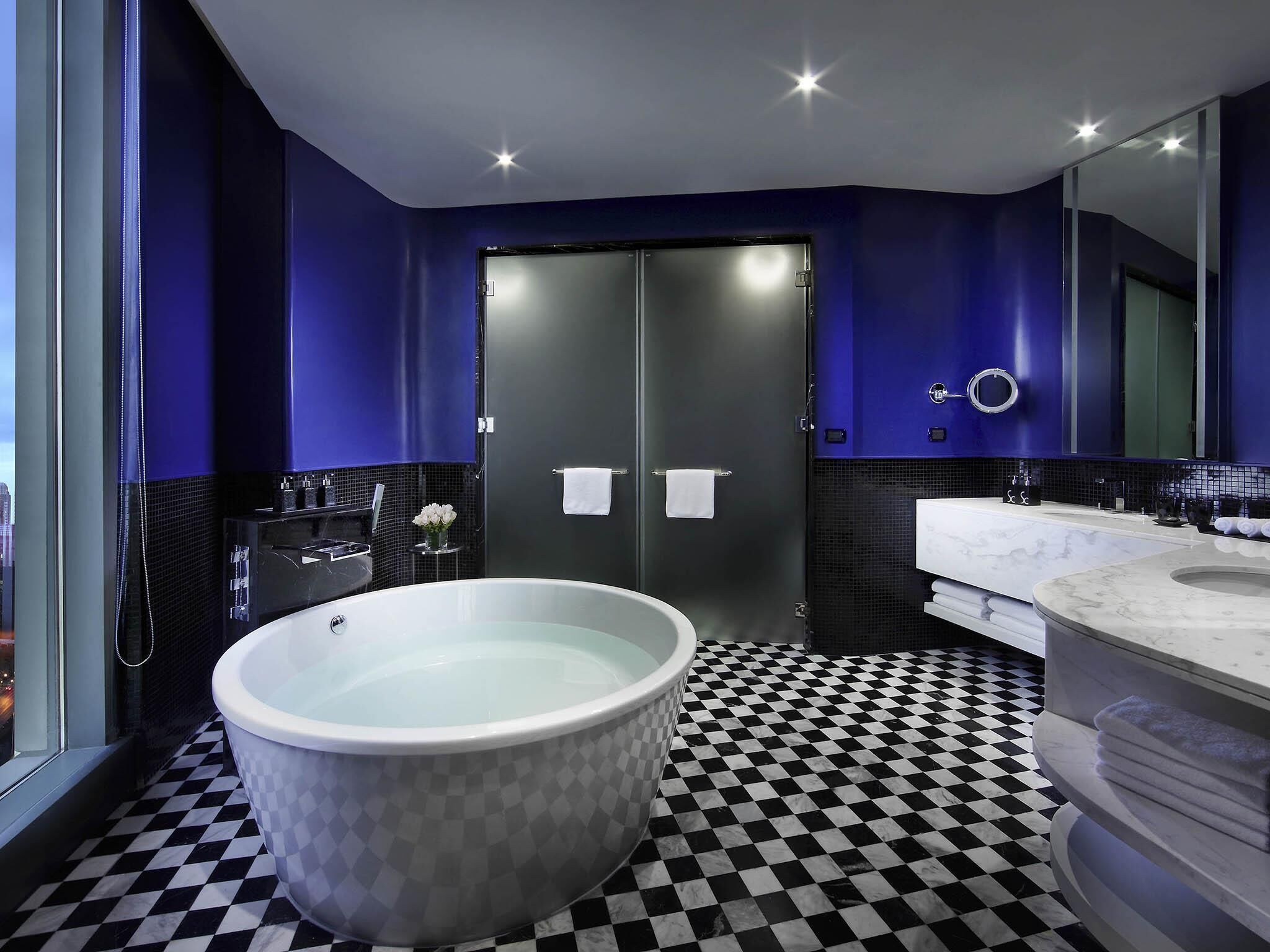 A modern bathroom with a freestanding bathtub, a large mirror, and a checkered floor.