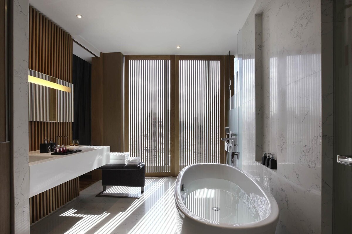 A modern bathroom with a freestanding bathtub, a vanity with a mirror, and a large window with vertical blinds.