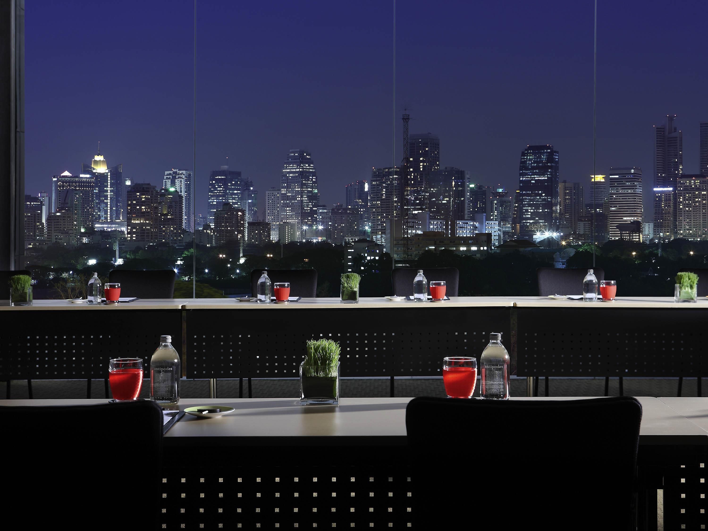Un restaurant offrant une vue sur les toits de la ville, des tables ornées de verres rouges et une plante en pot.