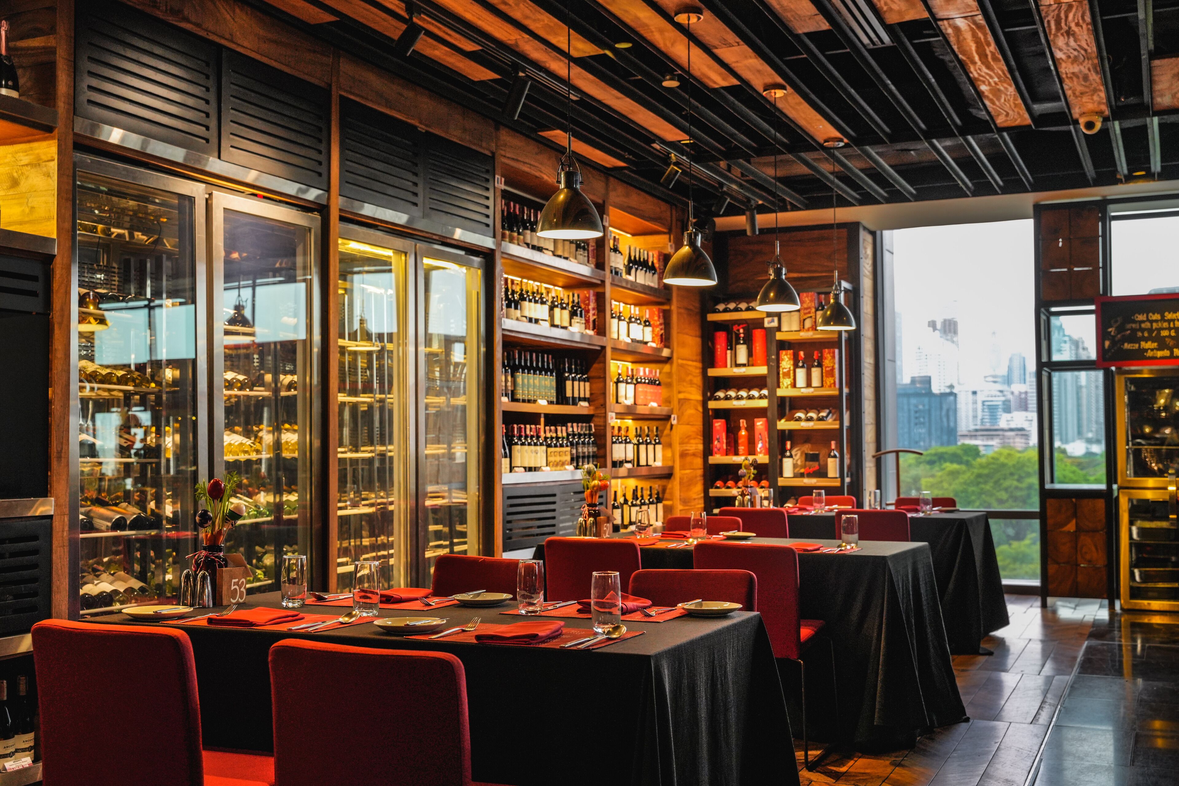 Ein Restaurant mit gedeckten Tischen, Weinflaschen an Regalen und Blick auf die Stadt durch große Fenster.
