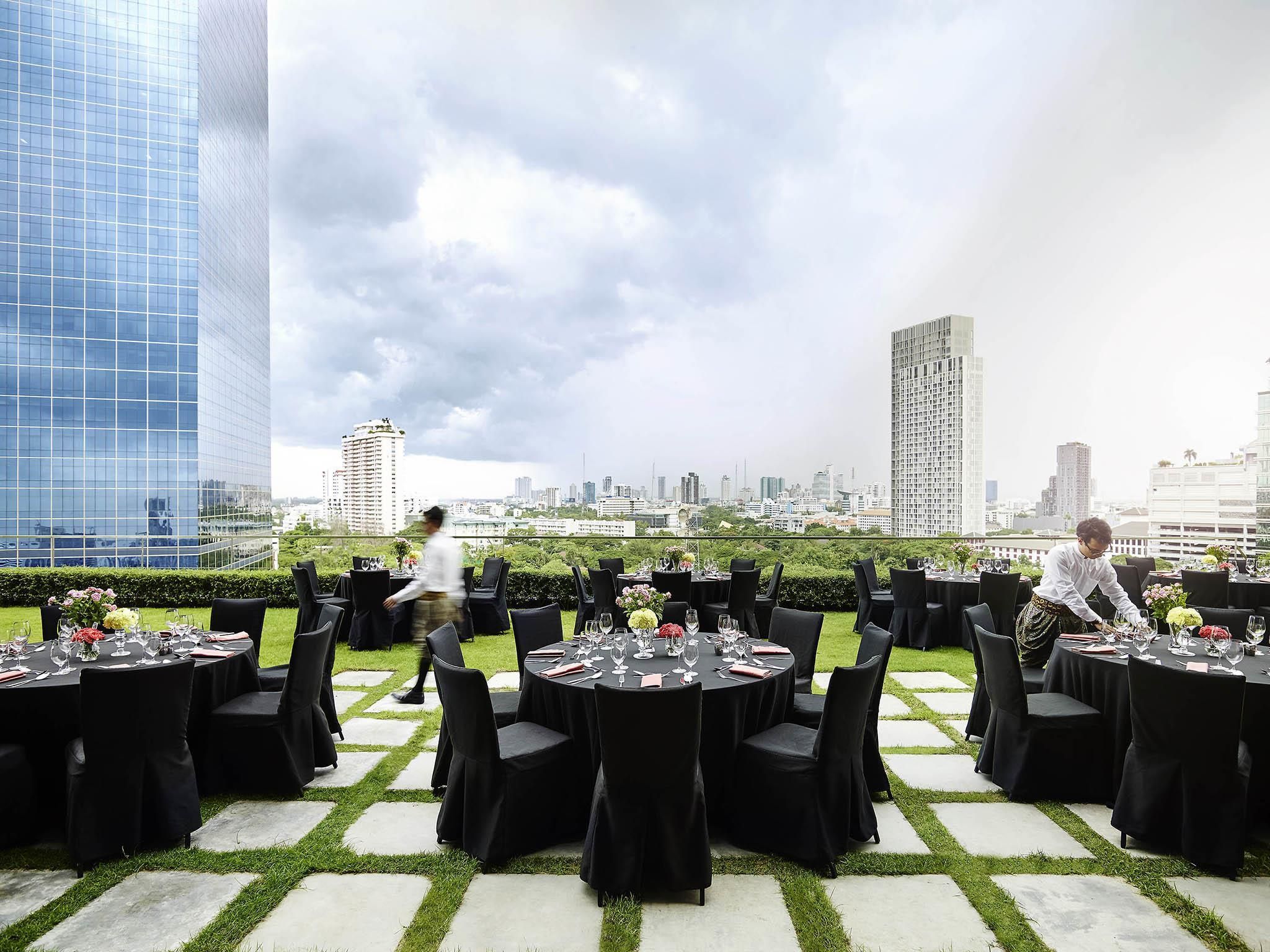Un espace de restauration en plein air avec des tables dressées pour un repas, entouré d’immeubles de la ville.