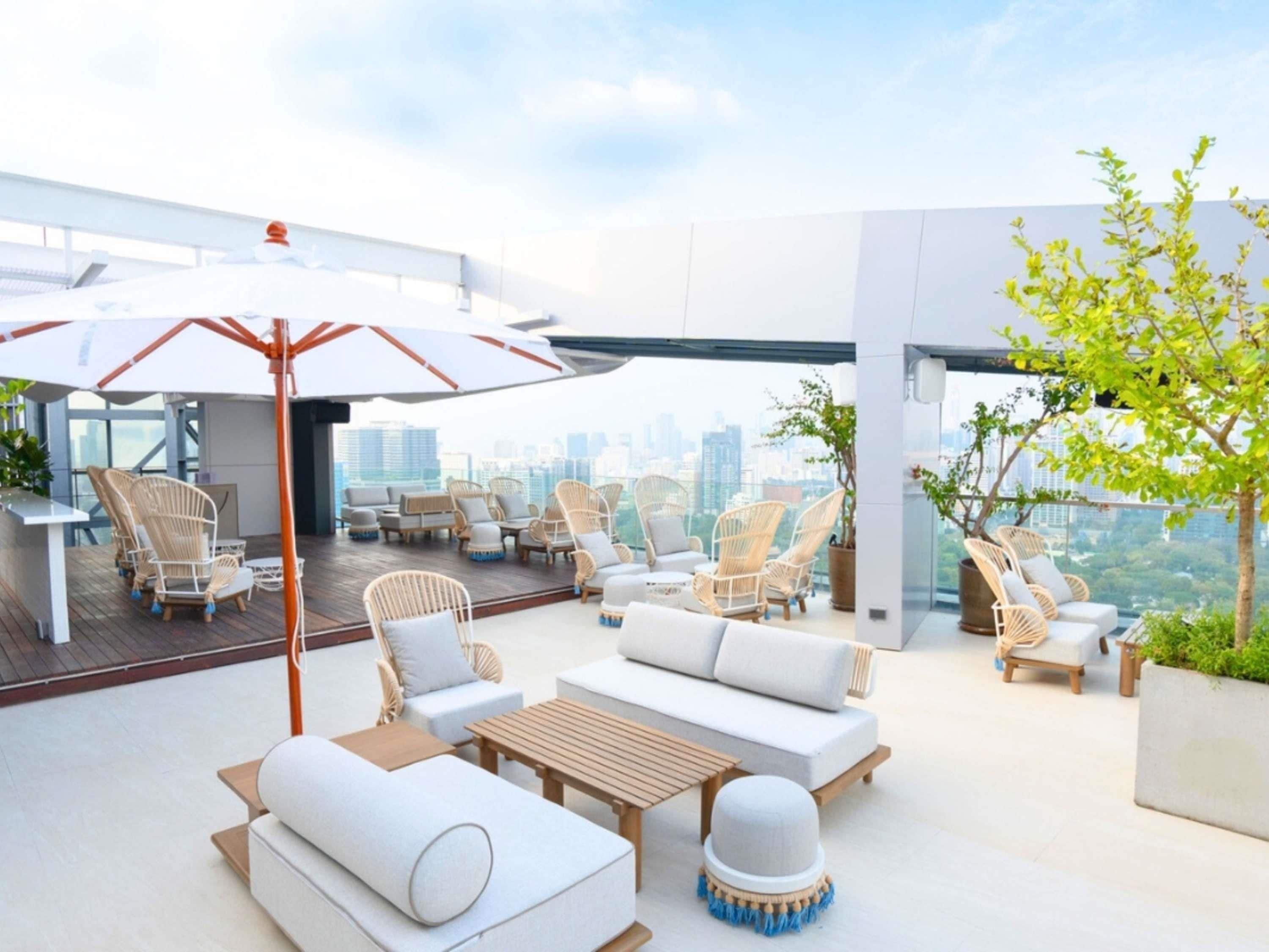 A rooftop lounge with wicker furniture, a wooden table, and a large umbrella.