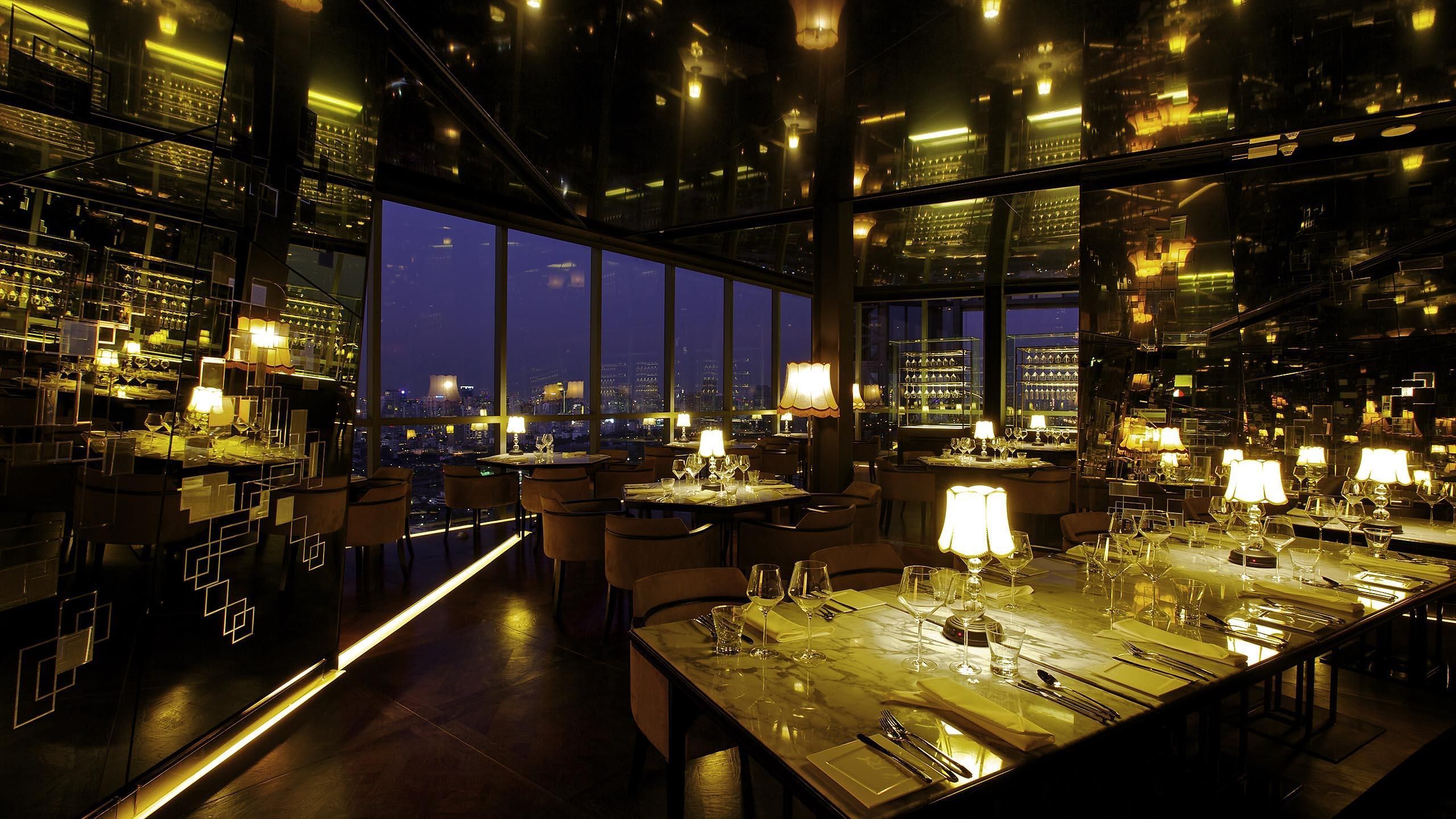 A high-rise restaurant with multiple dining tables, large windows offering city views, and a modern interior design.
