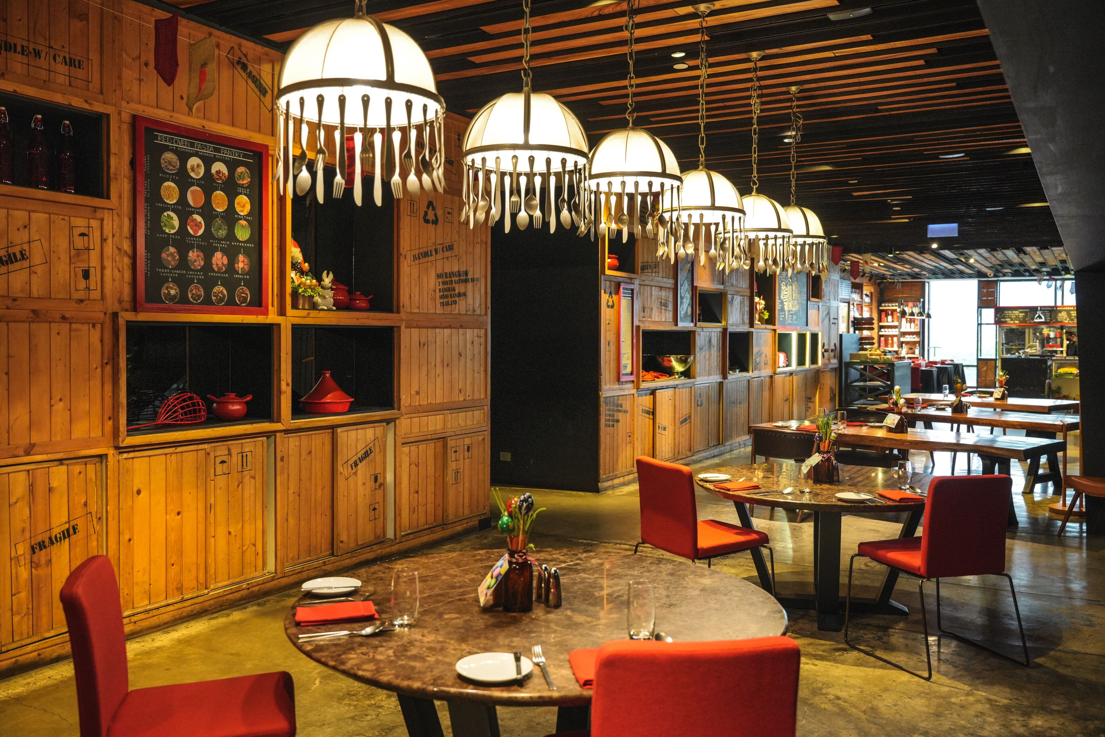 A restaurant with wooden walls, hanging pendant lights, and red chairs.