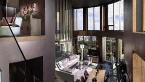 A modern interior with a curved staircase, a seating area with a sofa and chairs, and large windows offering a city view. - SO/ Bangkok (Bangkok)
