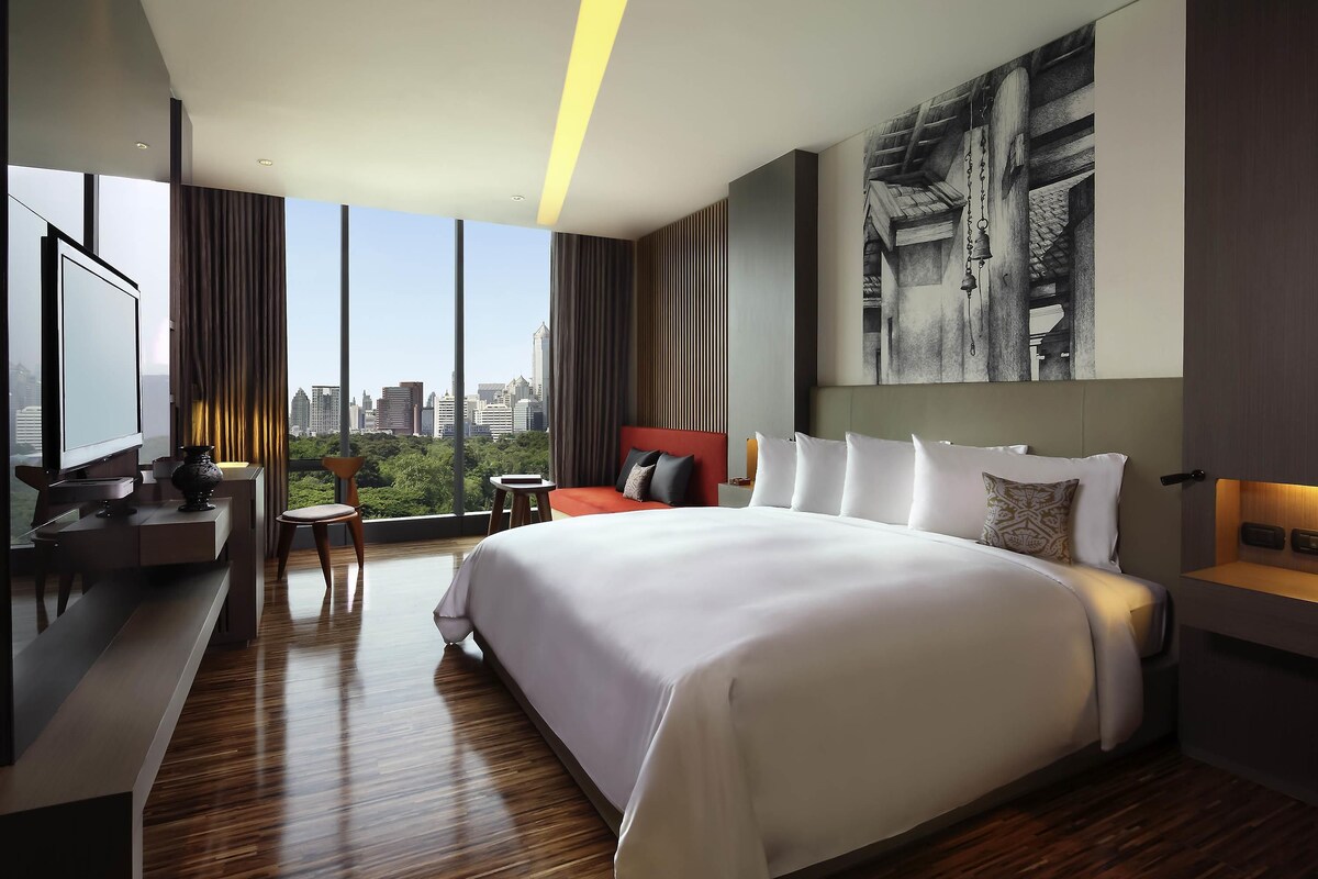 A modern hotel room with a large bed, a TV, a desk, and a city view.