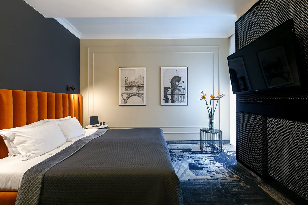 A modern hotel room with a large bed, a television, and two framed artworks on the wall.