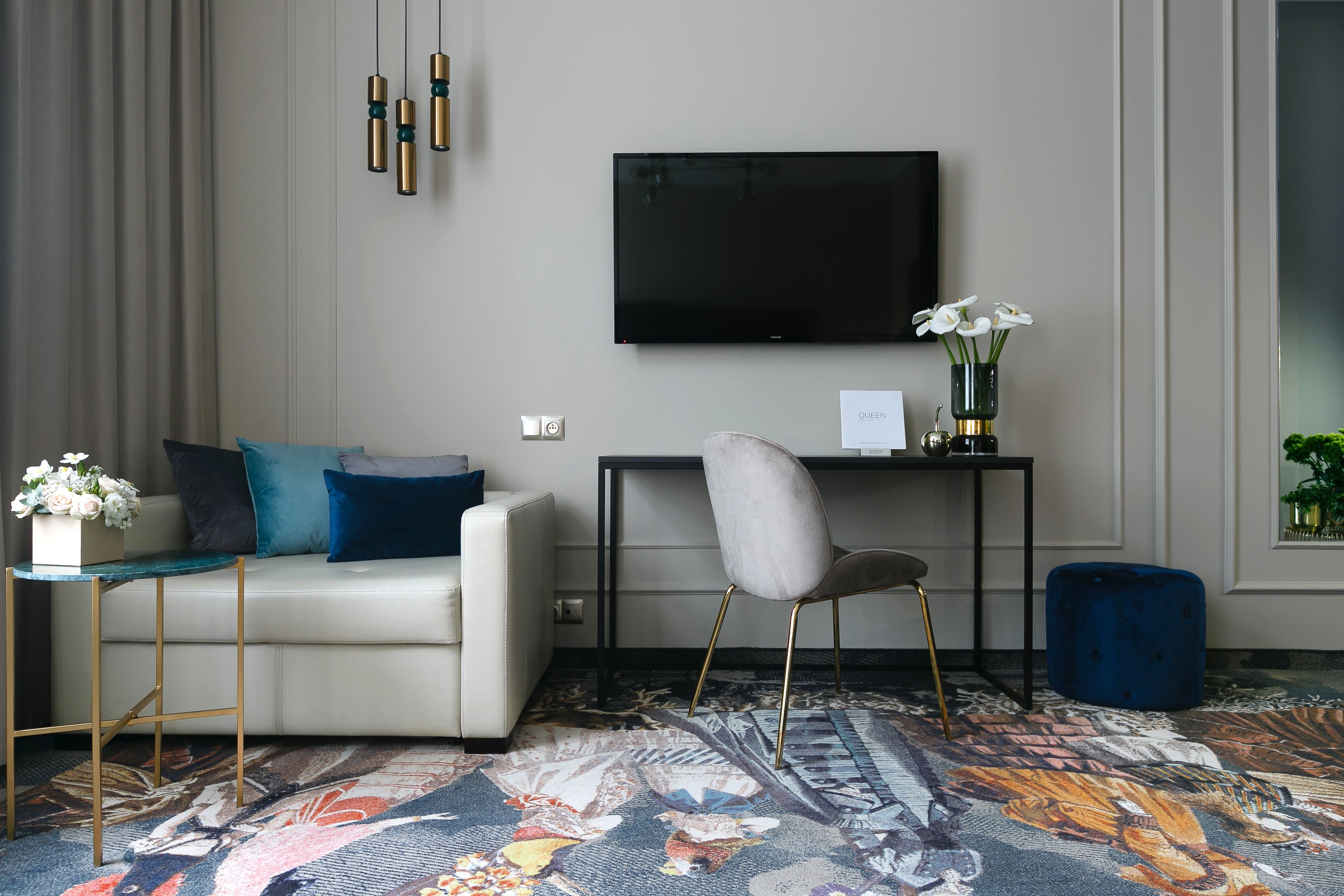 A modern living room with a sofa, a chair, a flat-screen TV, a small table, and a decorative vase with flowers.