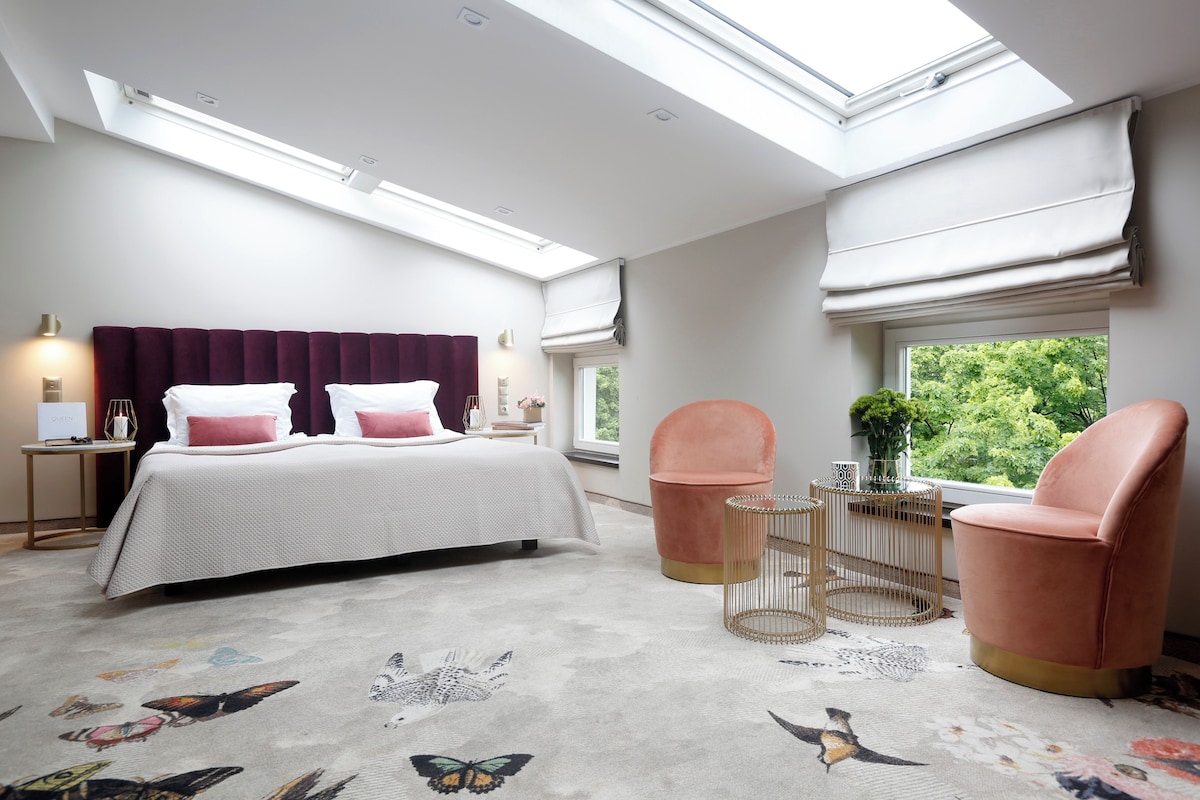 A bedroom with a bed, two chairs, a small table, a window with a view, and a skylight.