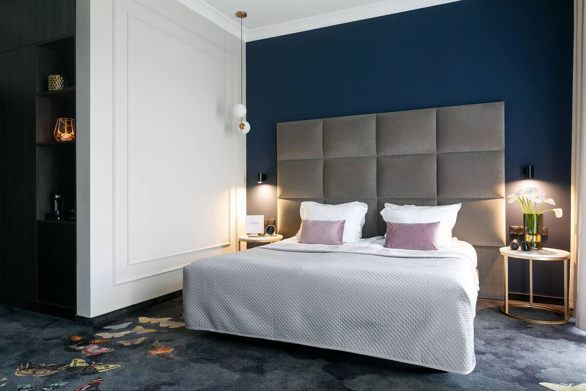 A neatly made bed with a grey headboard, two bedside tables with lamps, and a floral carpet pattern.