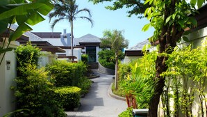 A narrow, tree-lined pathway leading to a modern house with a sloped roof and a small staircase. - Samui Resotel Beach Resort (Koh Samui)