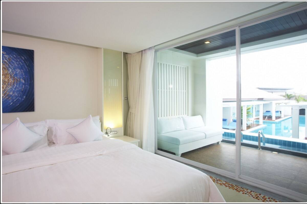 A hotel room with a large bed, a view of a swimming pool, and a balcony.