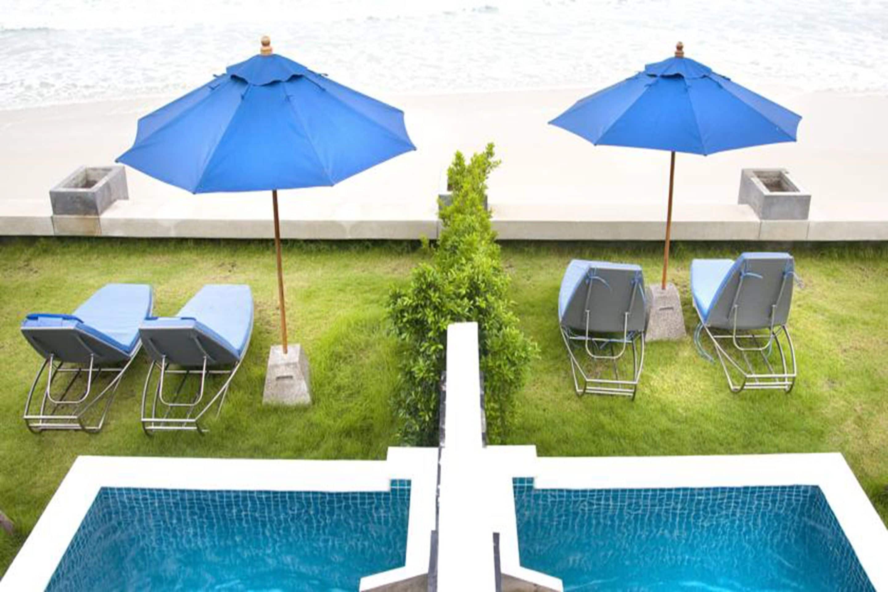 Un espace piscine agrémenté de deux parasols bleus, de deux chaises longues et offrant une vue sur l’océan.