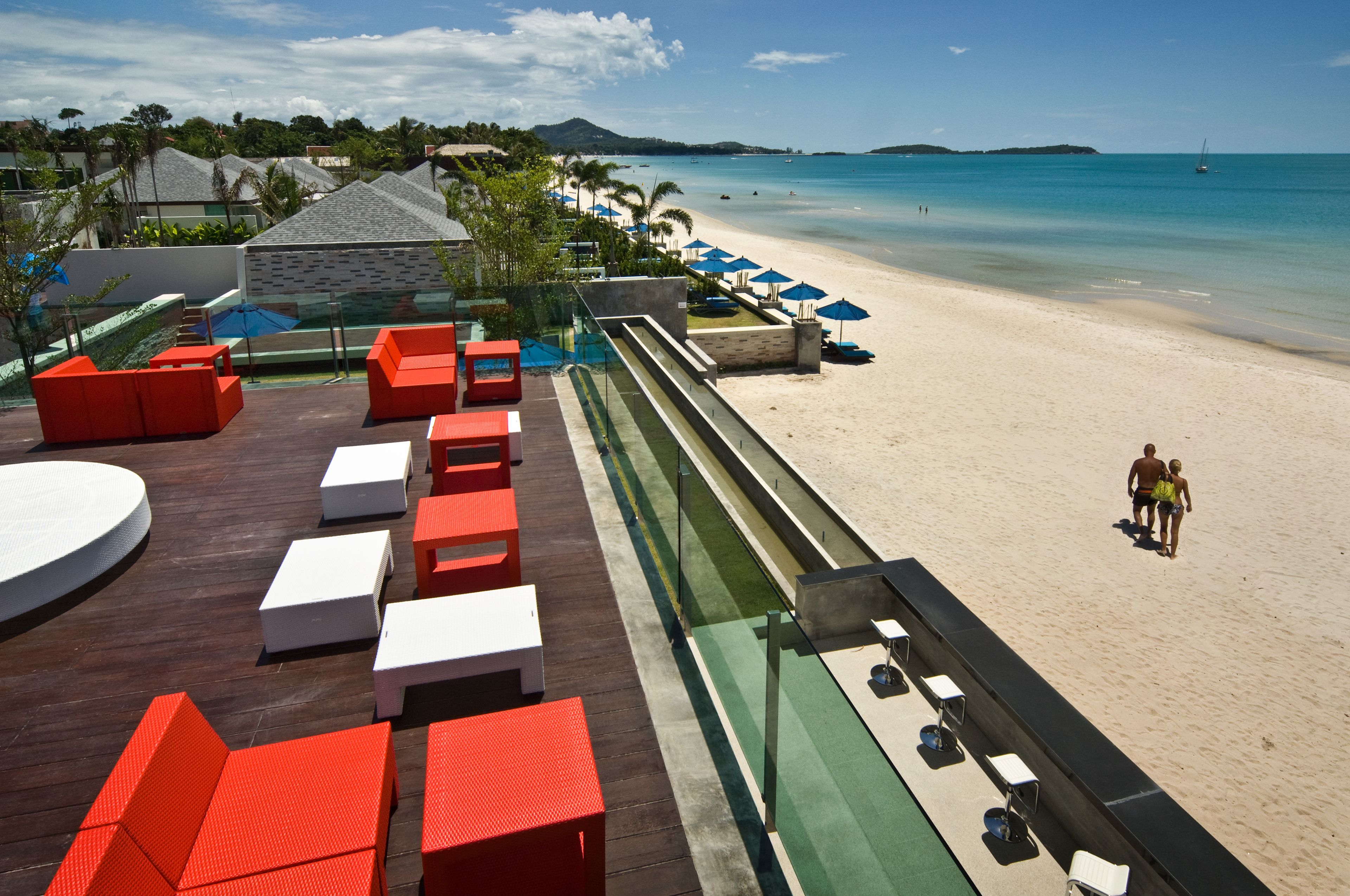 Un resort frente a la playa con zona de piscina que cuenta con sillas de descanso rojas y blancas, un tobogán de agua y vistas a la playa y al océano.