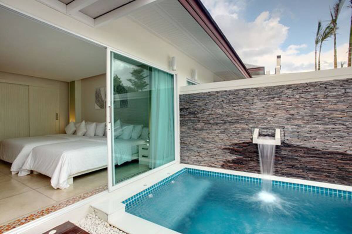 A modern bedroom with a glass door leading to a bathroom, a small pool with a waterfall feature, and a stone wall.
