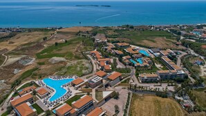 An aerial view of a resort with multiple buildings, a large swimming pool, and a view of the sea.