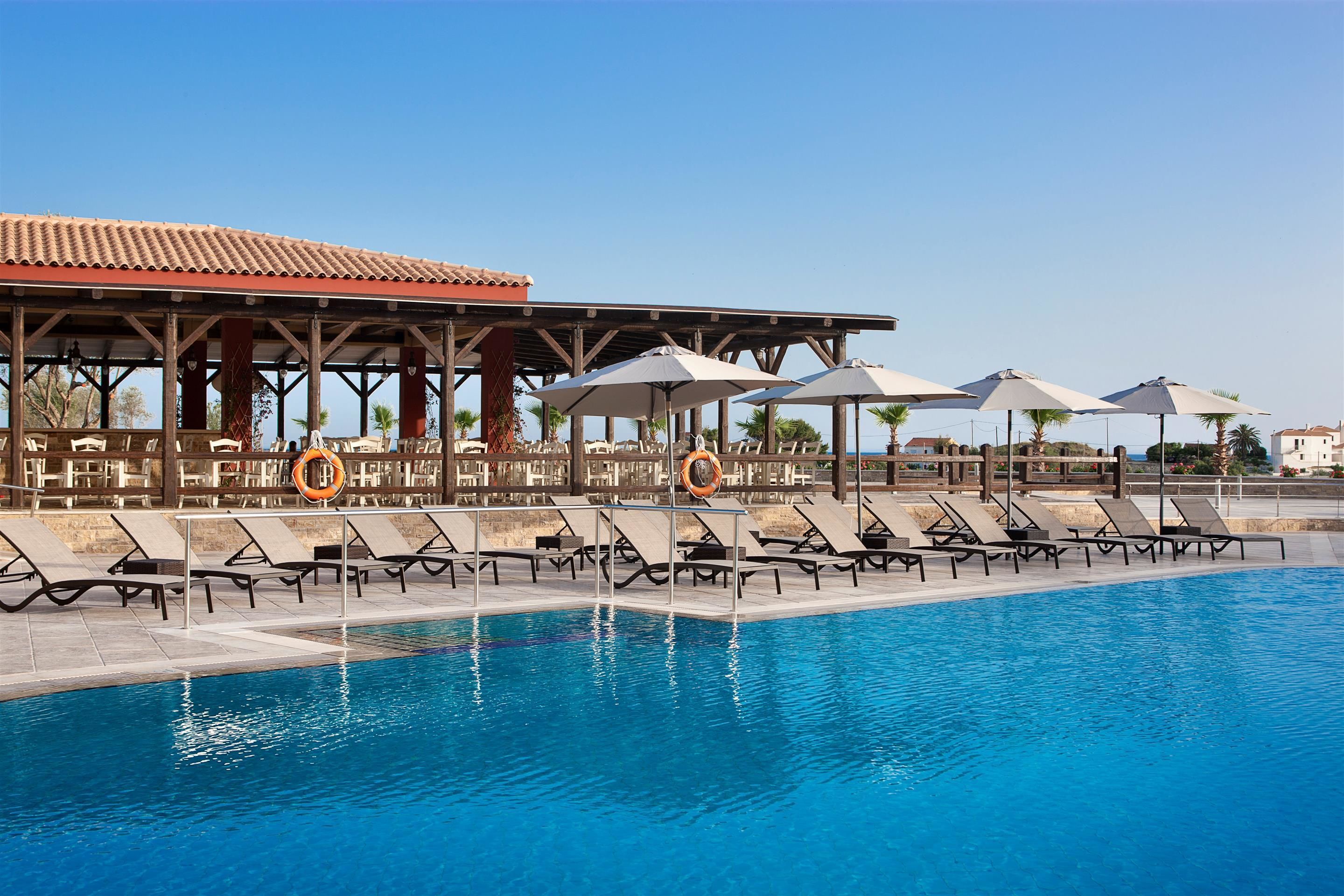 A swimming pool with sun loungers and umbrellas, a covered seating area, and lifebuoys.