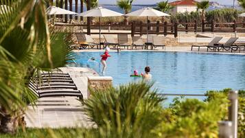 Relax by the serene pool surrounded by lounge chairs and umbrellas, with a shaded seating area nearby.