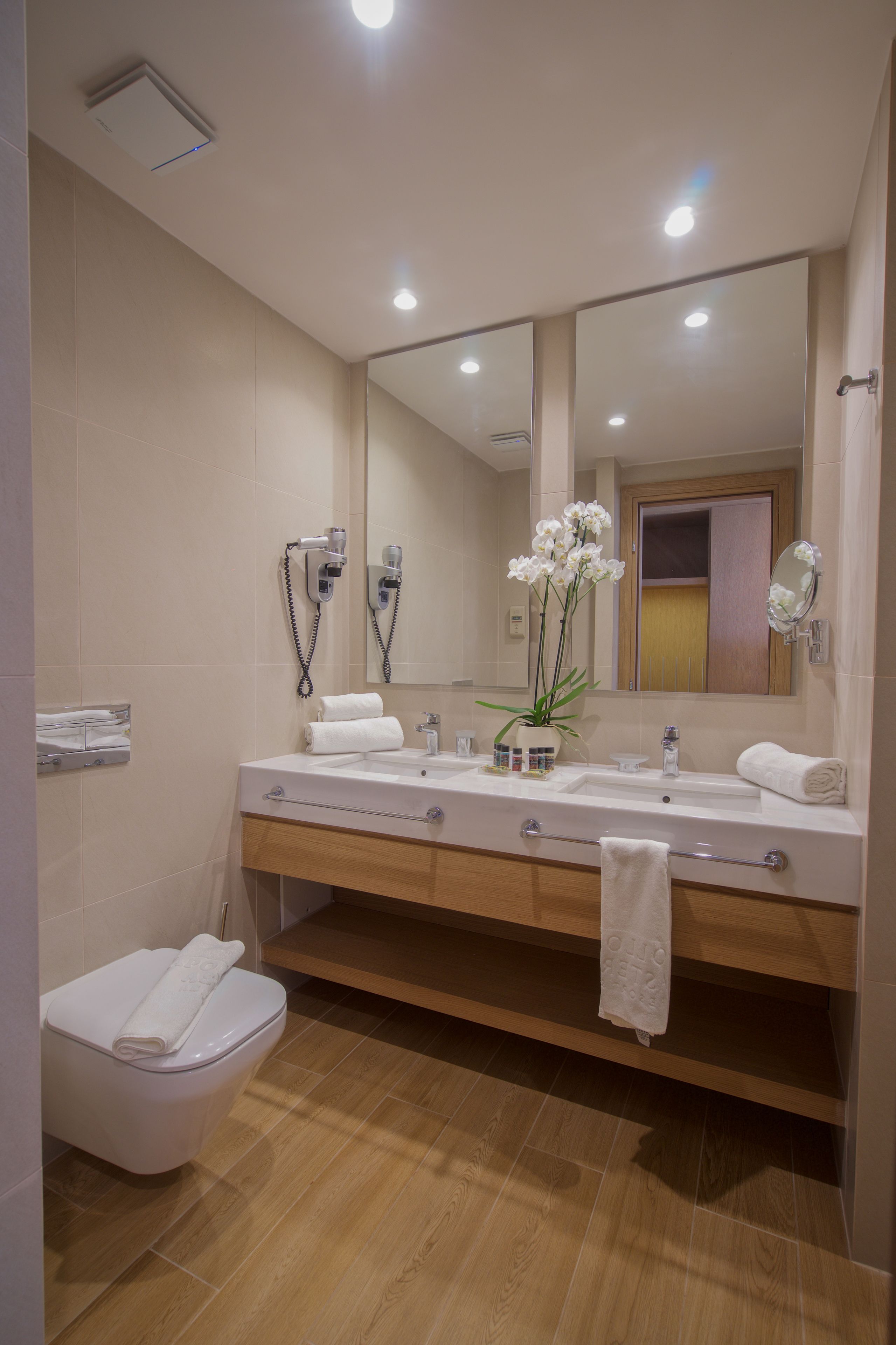 A modern bathroom with a wooden vanity, two sinks, a large mirror, and a toilet.