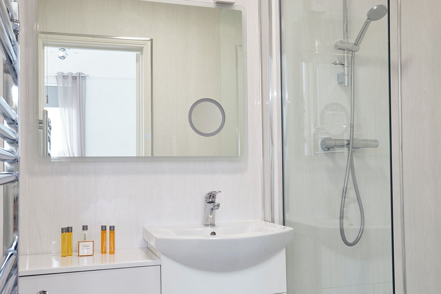 Ein Badezimmer mit einem weißen Waschbecken, einem Spiegel und einer Duschkabine.