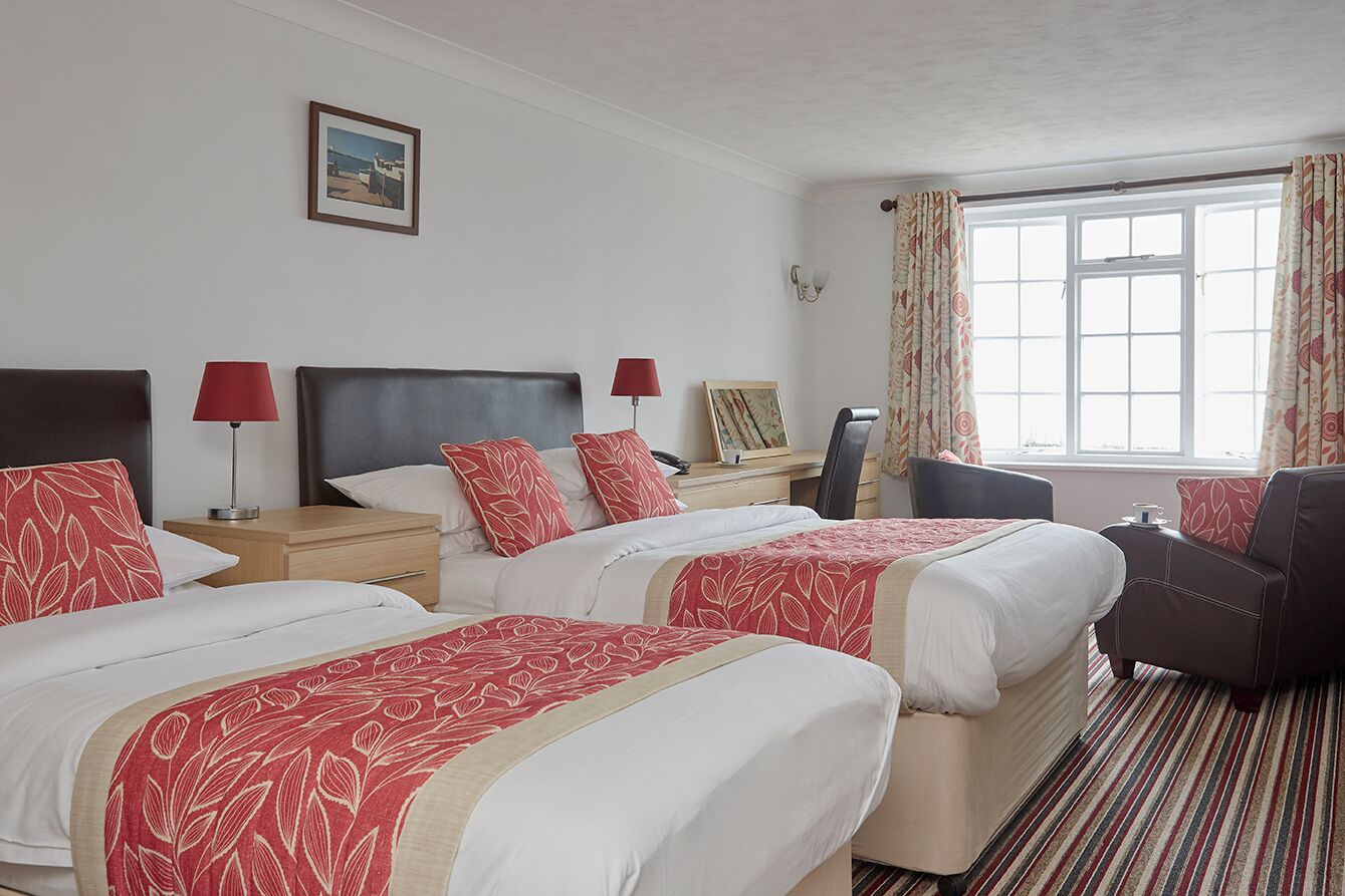 A hotel room with two beds, a desk, a chair, and a large window with curtains.