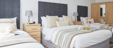 A hotel room with two beds, a wardrobe, bedside tables with lamps, and a mirror.